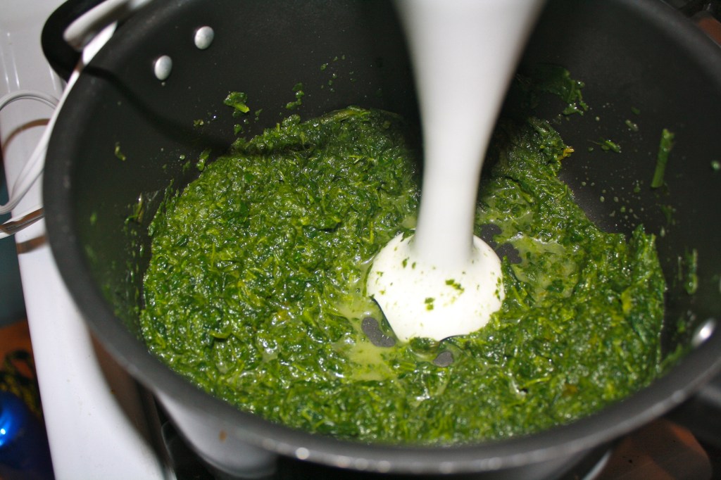 Using an immersion blender to blend the chopped spinach into a creamy, smooth texture.